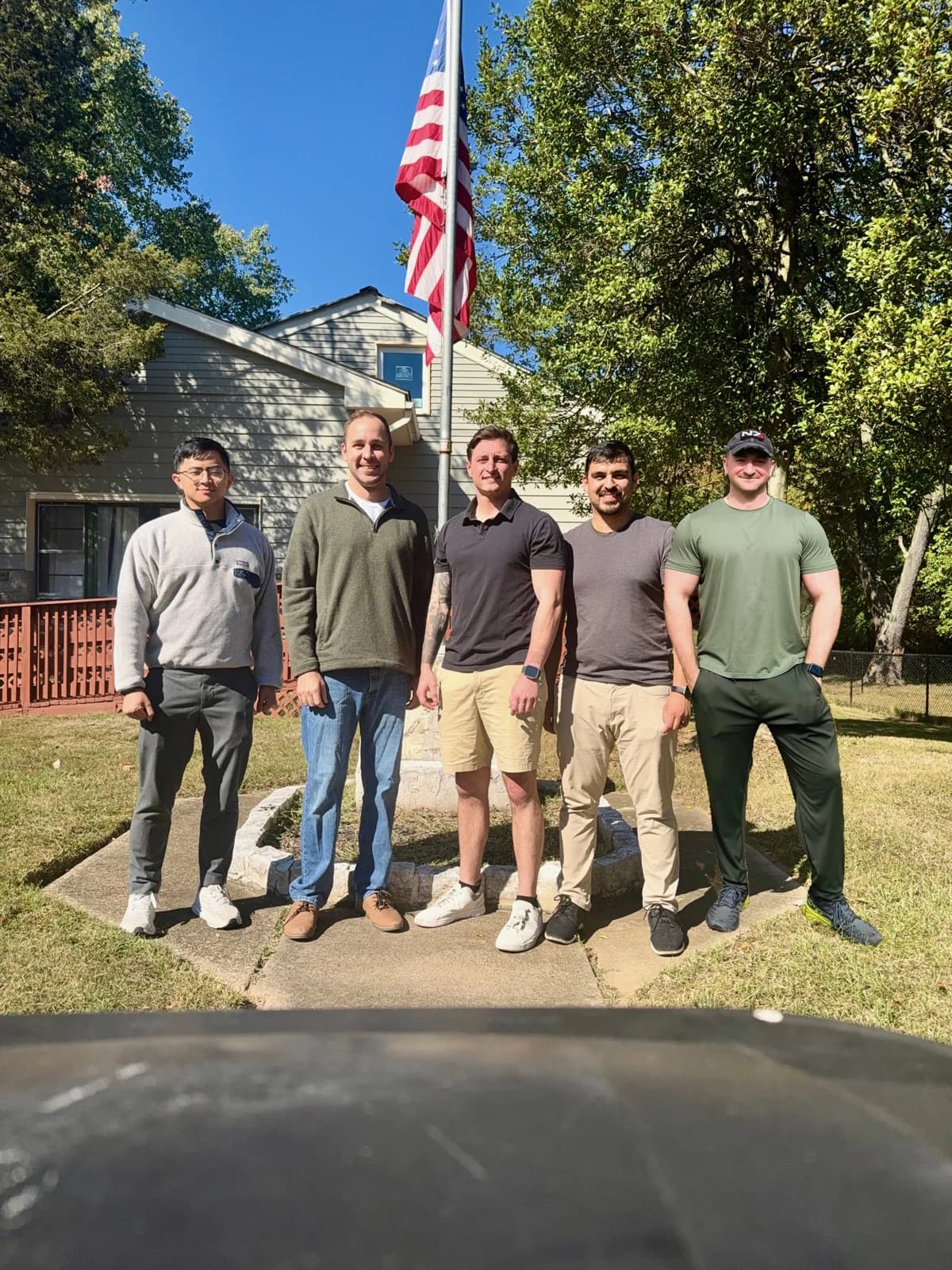 Five people standing outside a house beneath an American flag.