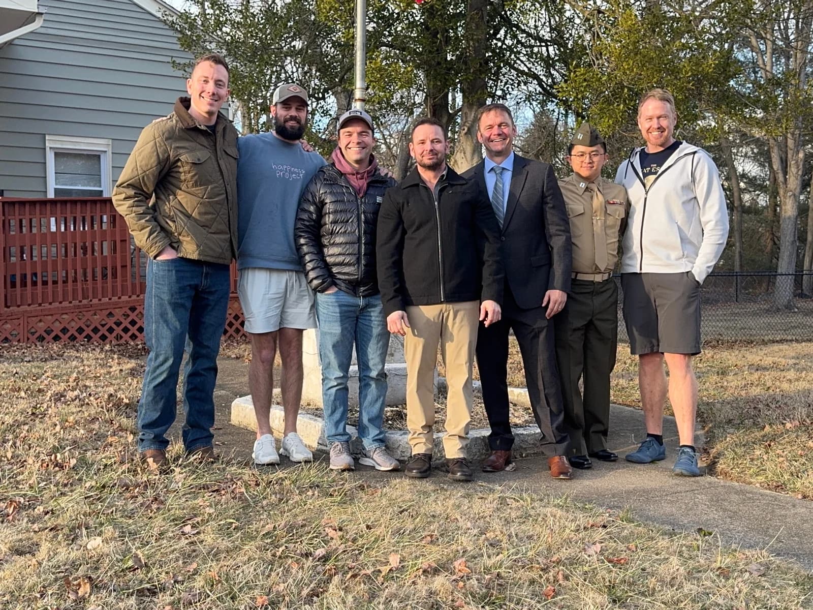 Seven people standing together outdoors beside a house.