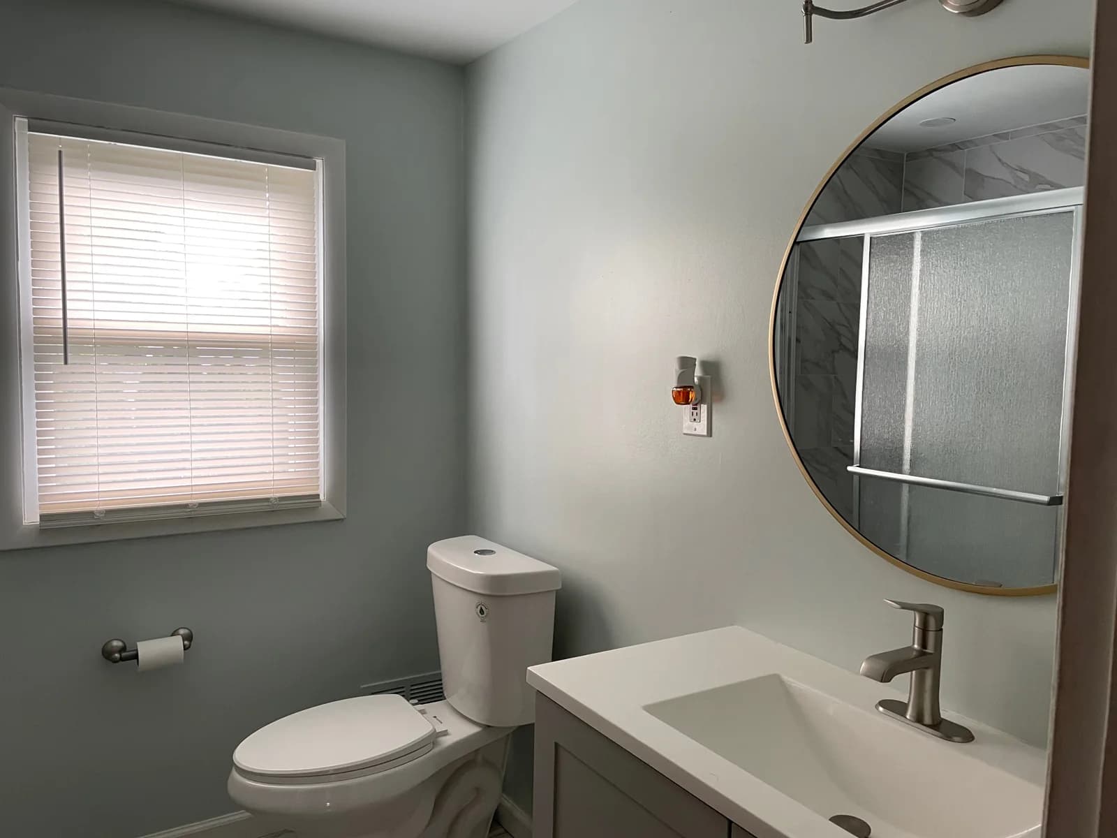 Bathroom with a white vanity, round mirror, and shower reflected in the mirror.