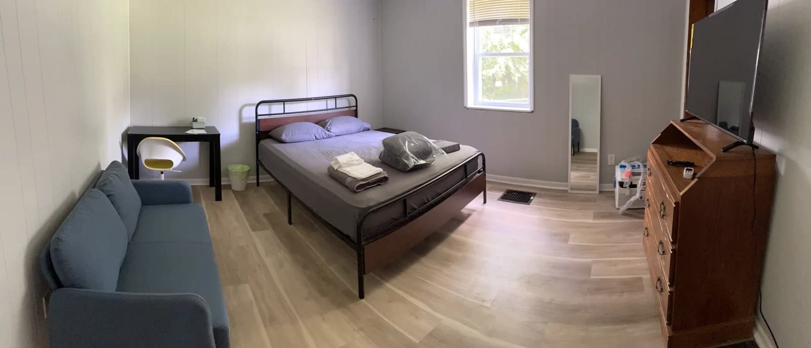 Furnished bedroom with a bed, sofa, desk, and television.