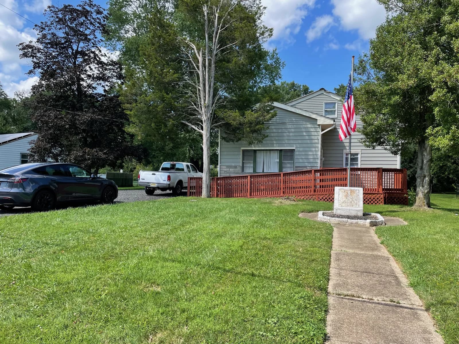 House exterior with a red deck, green lawn, and American flag.